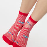 Woman wearing a red and white striped ankle grip sock with sardines swimming around the sock. Made for pilates, barre, yoga, and beyond. 