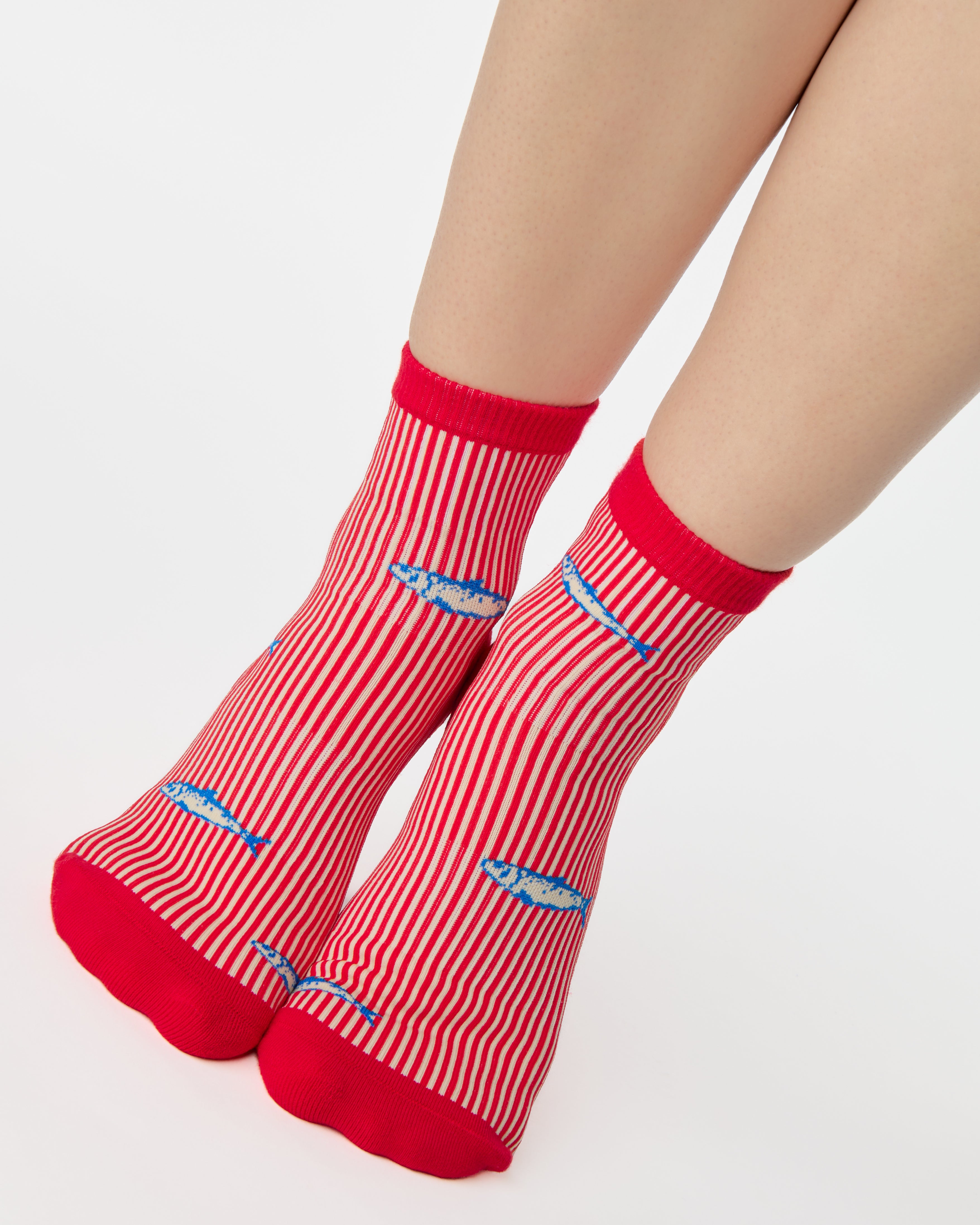 Woman wearing a red and white striped ankle grip sock with sardines swimming around the sock. Made for pilates, barre, yoga, and beyond. 
