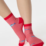 Woman wearing a red and white striped ankle grip sock with sardines swimming around the sock. Made for pilates, barre, yoga, and beyond. 