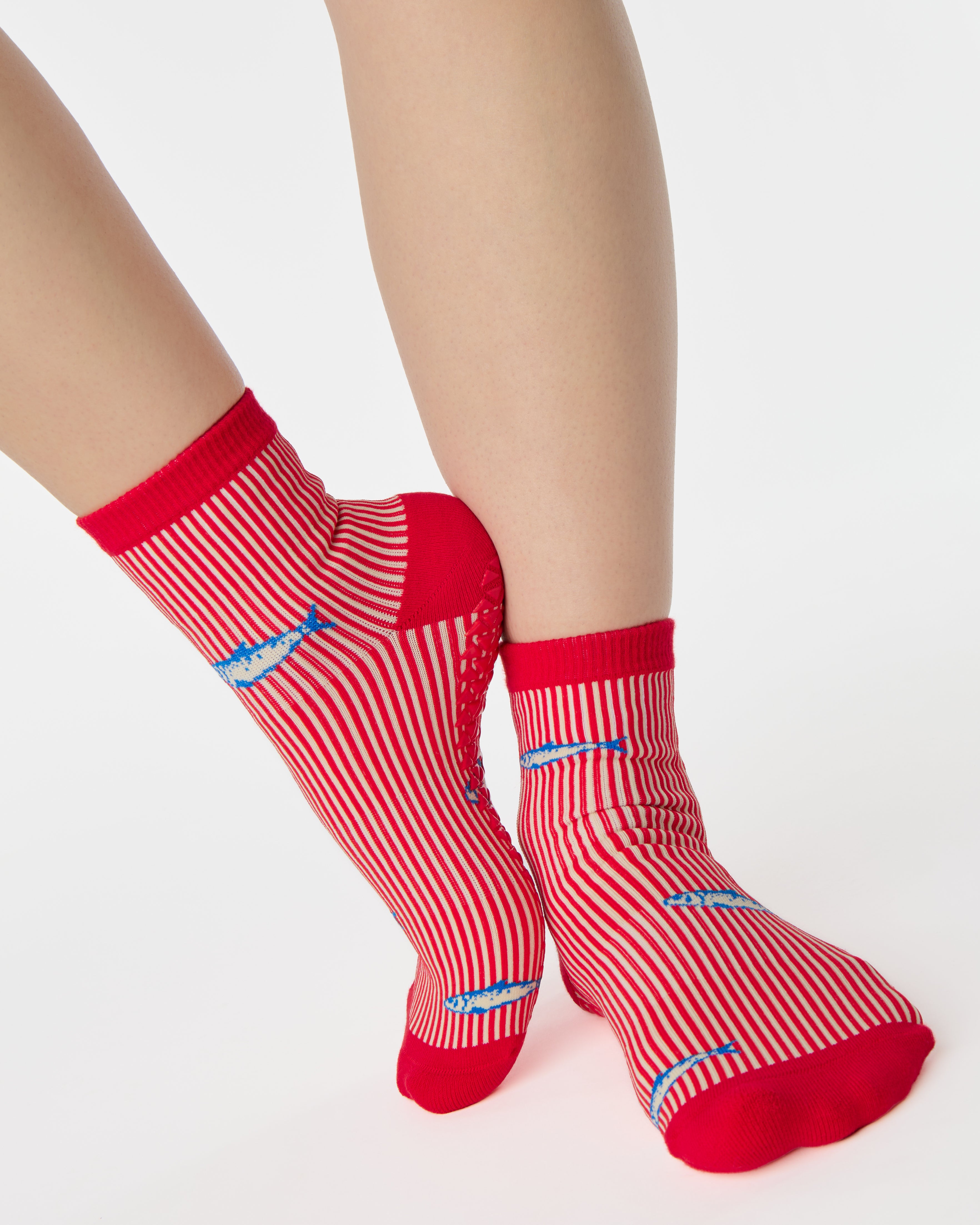 Woman wearing a red and white striped ankle grip sock with sardines swimming around the sock. Made for pilates, barre, yoga, and beyond. 