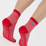 Woman wearing a red and white striped ankle grip sock with sardines swimming around the sock. Made for pilates, barre, yoga, and beyond. 