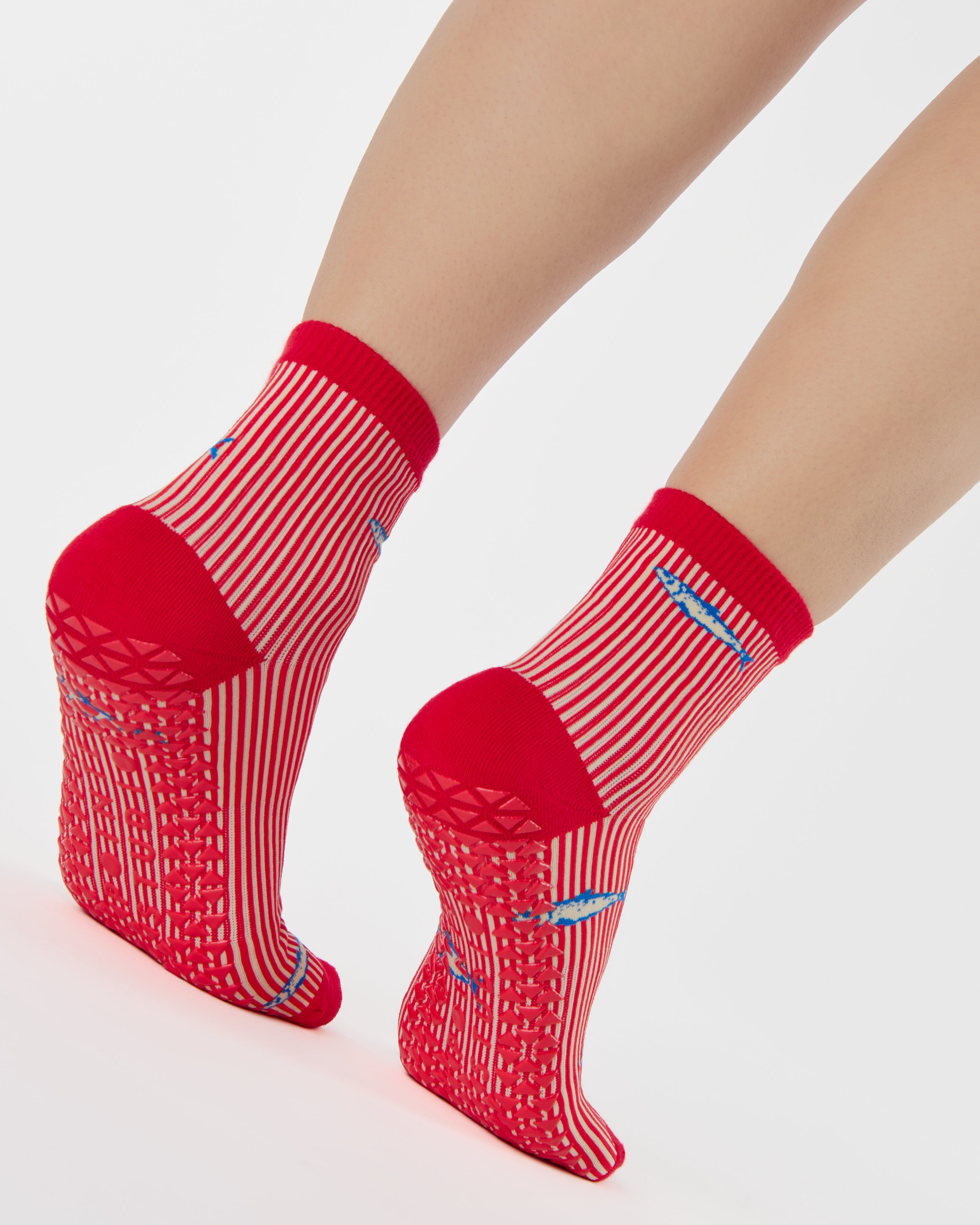 Woman wearing a red and white striped ankle grip sock with sardines swimming around the sock. Made for pilates, barre, yoga, and beyond. 