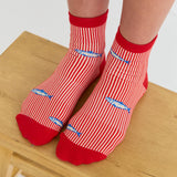 Woman wearing a red and white striped ankle grip sock with sardines swimming around the sock. Made for pilates, barre, yoga, and beyond. 