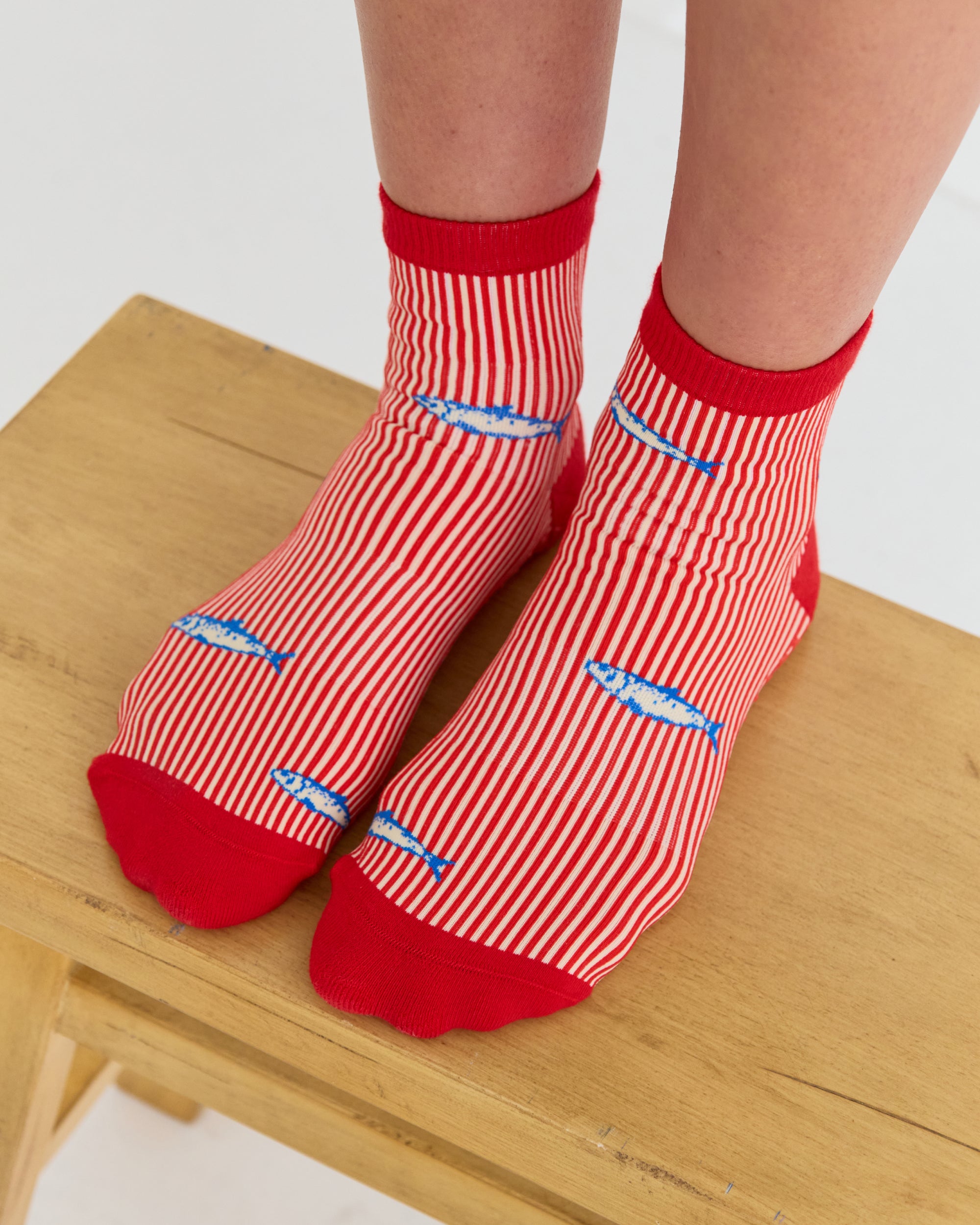 Woman wearing a red and white striped ankle grip sock with sardines swimming around the sock. Made for pilates, barre, yoga, and beyond. 