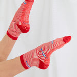 Woman wearing a red and white striped ankle grip sock with sardines swimming around the sock. Made for pilates, barre, yoga, and beyond. 