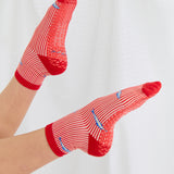 Woman wearing a red and white striped ankle grip sock with sardines swimming around the sock. Made for pilates, barre, yoga, and beyond. 