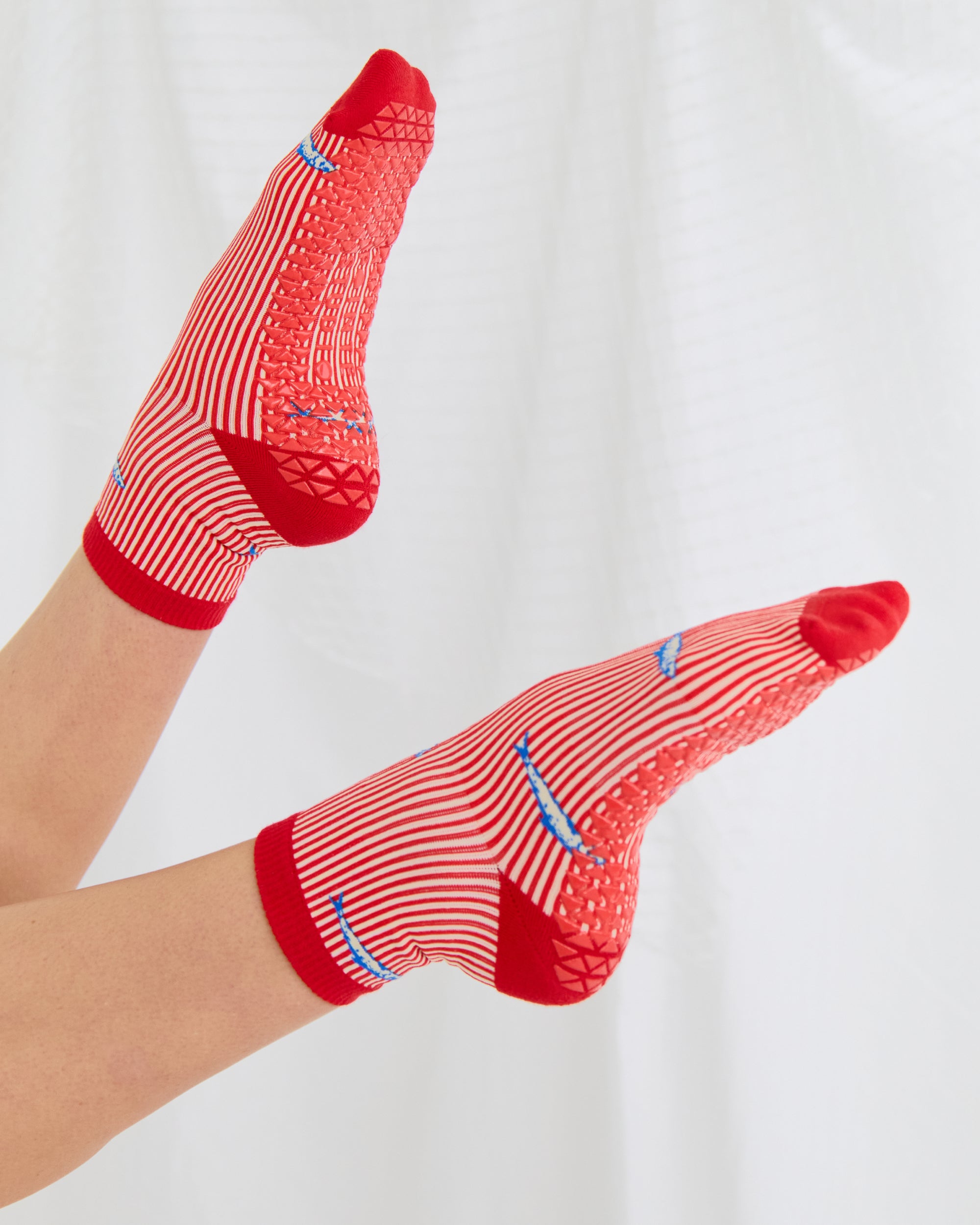 Woman wearing a red and white striped ankle grip sock with sardines swimming around the sock. Made for pilates, barre, yoga, and beyond. 