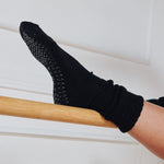 Women wearing a black mid-weight knit grip sock that scrunches, made for Pilates, Barre, Yoga, and Beyond. 