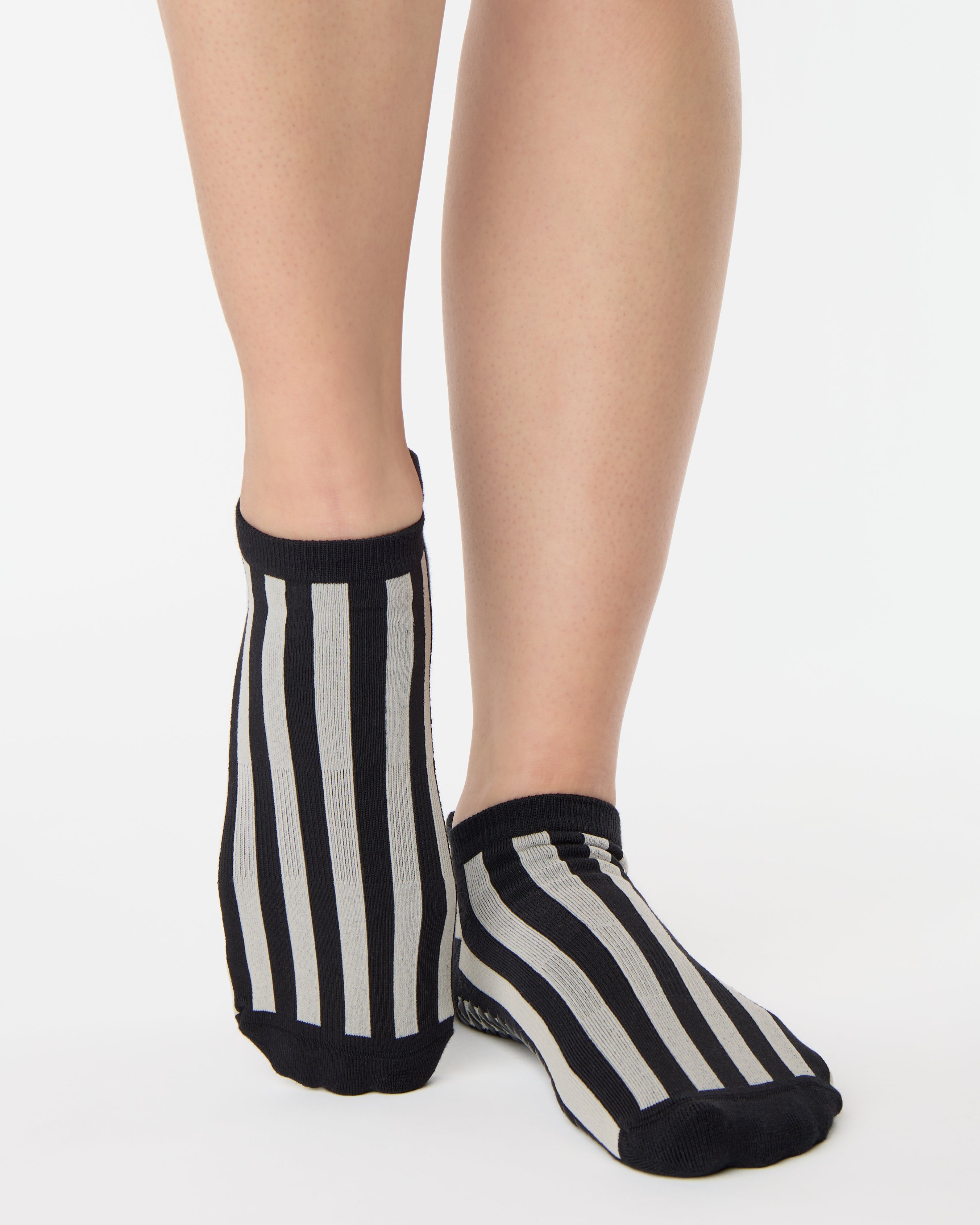 Women wearing a black and grey stripped full foot pilates grip sock, made for pilates, barre, yoga, and beyond.
