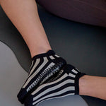 Women on yoga mat wearing a black and grey stripped full foot pilates grip sock, made for pilates, barre, yoga, and beyond.