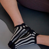 Women on yoga mat wearing a black and grey stripped full foot pilates grip sock, made for pilates, barre, yoga, and beyond.