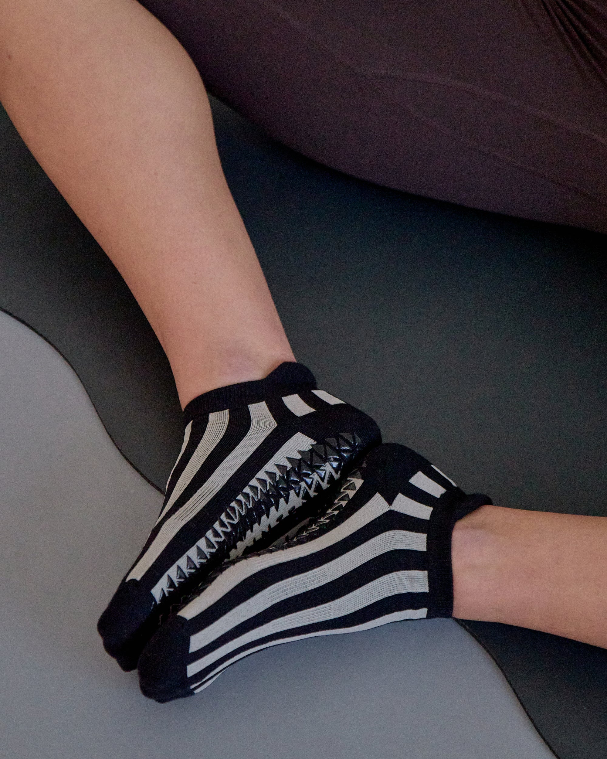 Women on yoga mat wearing a black and grey stripped full foot pilates grip sock, made for pilates, barre, yoga, and beyond.