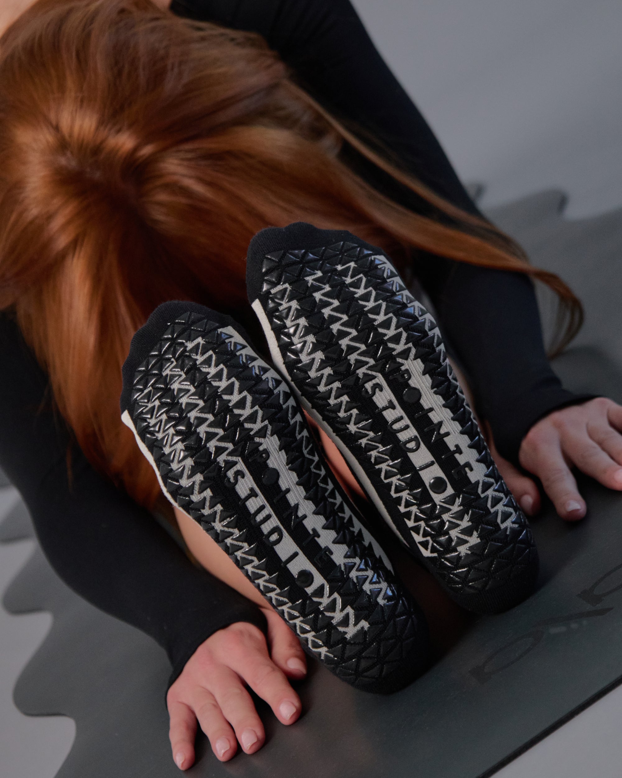 Women on a yoga mat wearing a black and grey stripped full foot pilates grip sock, made for pilates, barre, yoga, and beyond.