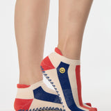 Woman wearing a playfully blue, white, and red stripped full foot grip sock with a little embroidered smiley face by the ankle. Made for pilates, barre, yoga, and beyond. 
