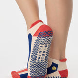 Woman wearing a playfully blue, white, and red stripped full foot grip sock with a little embroidered smiley face by the ankle. Made for pilates, barre, yoga, and beyond. 