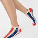 Woman wearing a playfully blue, white, and red stripped full foot grip sock with a little embroidered smiley face by the ankle. Made for pilates, barre, yoga, and beyond. 