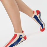 Woman wearing a playfully blue, white, and red stripped full foot grip sock with a little embroidered smiley face by the ankle. Made for pilates, barre, yoga, and beyond. 