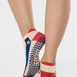Woman wearing a playfully blue, white, and red stripped full foot grip sock with a little embroidered smiley face by the ankle. Made for pilates, barre, yoga, and beyond. 