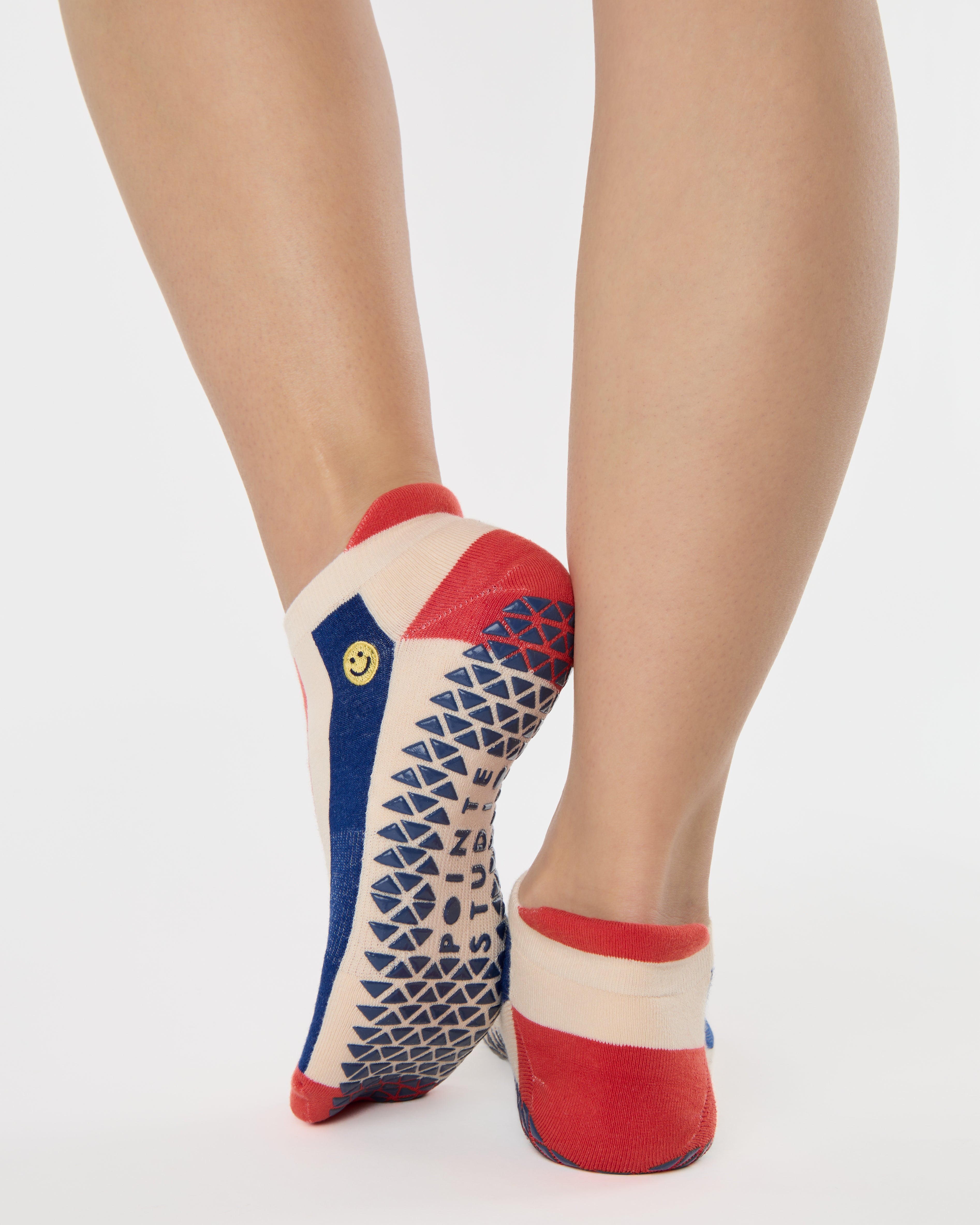 Woman wearing a playfully blue, white, and red stripped full foot grip sock with a little embroidered smiley face by the ankle. Made for pilates, barre, yoga, and beyond. 