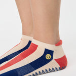 Woman wearing a playfully blue, white, and red stripped full foot grip sock with a little embroidered smiley face by the ankle. Made for pilates, barre, yoga, and beyond. 