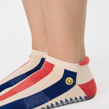 Woman wearing a playfully blue, white, and red stripped full foot grip sock with a little embroidered smiley face by the ankle. Made for pilates, barre, yoga, and beyond. 