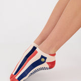 Woman wearing a playfully blue, white, and red stripped full foot grip sock with a little embroidered smiley face by the ankle. Made for pilates, barre, yoga, and beyond. 
