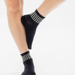 Women wearing a black ankle grip sock with white rows of hearts circling the top ankle made for Pilates, Barre, Yoga, and beyond. 