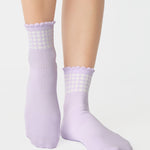 Women wearing a light purple ankle grip sock with white rows of hearts circling the top ankle made for Pilates, Barre, Yoga, and beyond. 