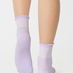 Women wearing a light purple ankle grip sock with white rows of hearts circling the top ankle made for Pilates, Barre, Yoga, and beyond. 