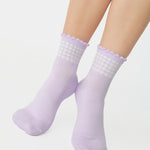 Women wearing a light purple ankle grip sock with white rows of hearts circling the top ankle made for Pilates, Barre, Yoga, and beyond. 