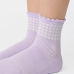 Women wearing a light purple ankle grip sock with white rows of hearts circling the top ankle made for Pilates, Barre, Yoga, and beyond. 