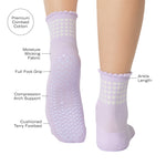 Women wearing a light purple ankle grip sock with white rows of hearts circling the top ankle made for Pilates, Barre, Yoga, and beyond with a list of product features.