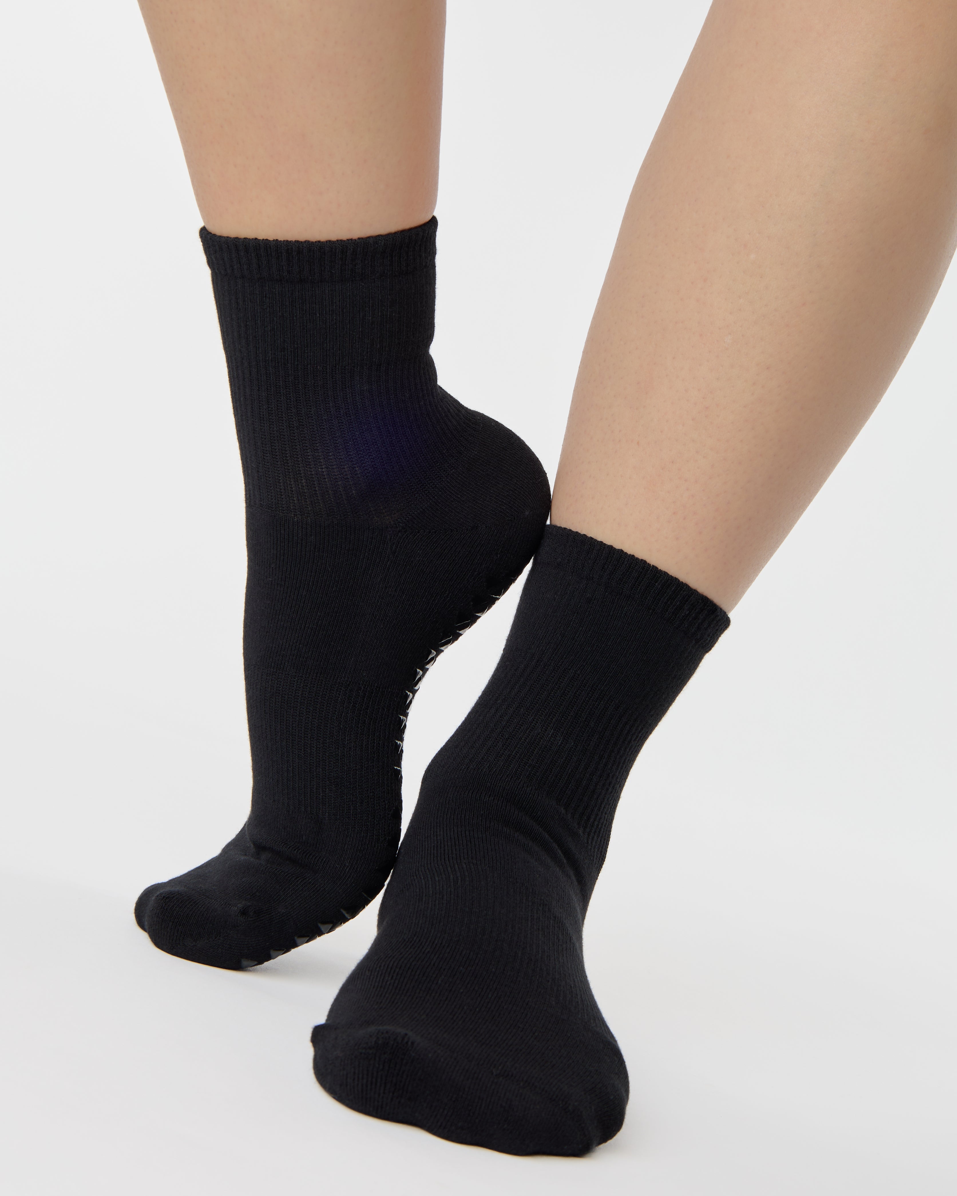 Women wearing a solid black ankle grip sock made for Pilates, Barre, Yoga, and beyond. 