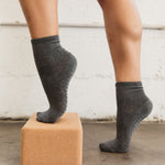 Women wearing a solid charcoal gray ankle grip sock made for Pilates, Barre, Yoga, and beyond. 