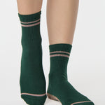 Woman wearing a solid green ankle grip sock with pink stripes on the toes and top ankle cuff made for Pilates, Barre, Yoga, and beyond. 