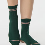 Woman wearing a solid green ankle grip sock with pink stripes on the toes and top ankle cuff made for Pilates, Barre, Yoga, and beyond. 