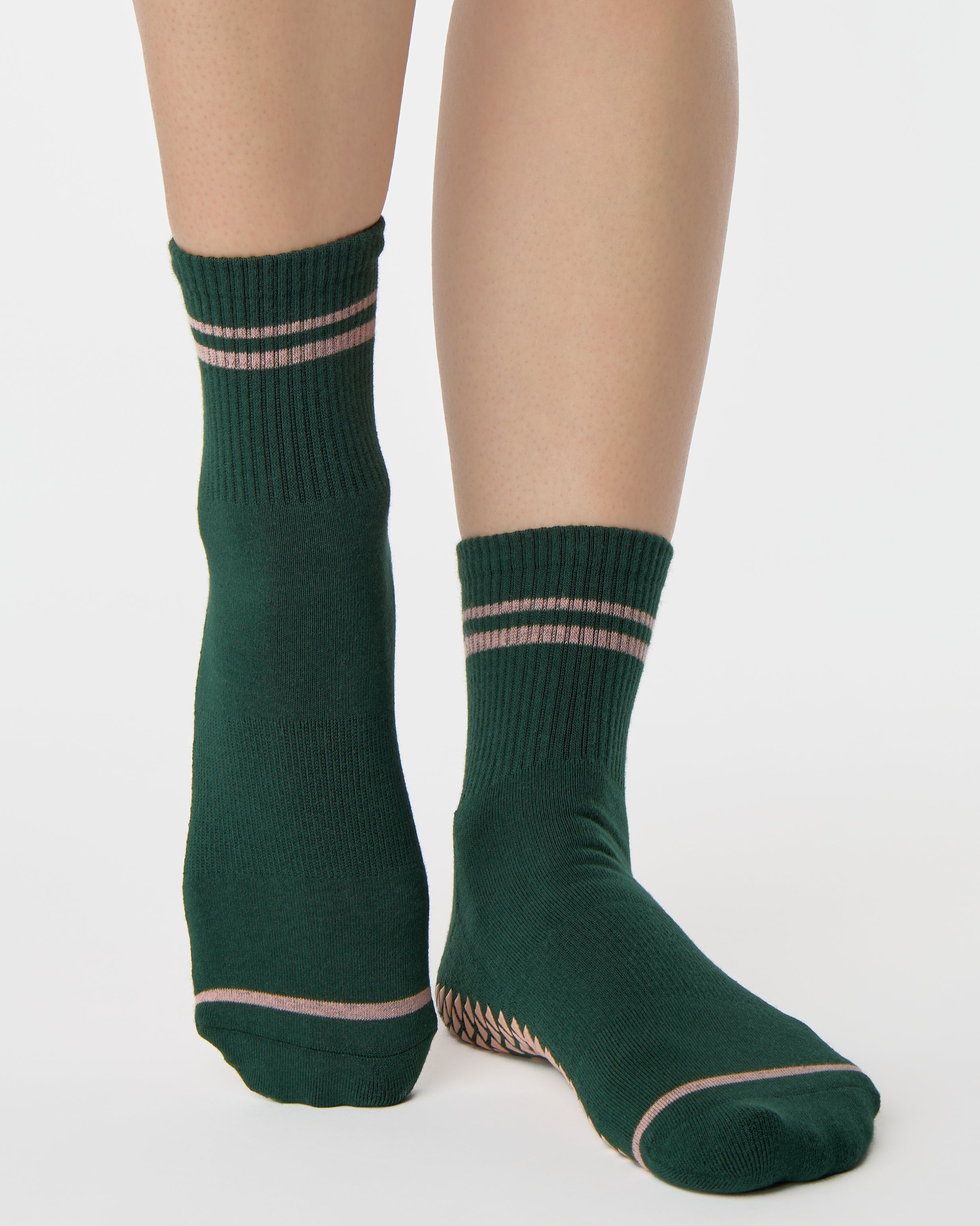 Woman wearing a solid green ankle grip sock with pink stripes on the toes and top ankle cuff made for Pilates, Barre, Yoga, and beyond. 