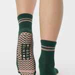 Woman wearing a solid green ankle grip sock with pink stripes on the toes and top ankle cuff made for Pilates, Barre, Yoga, and beyond. 
