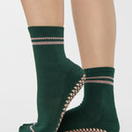 Woman wearing a solid green ankle grip sock with pink stripes on the toes and top ankle cuff made for Pilates, Barre, Yoga, and beyond. 