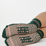 Woman wearing a solid green ankle grip sock with pink stripes on the toes and top ankle cuff made for Pilates, Barre, Yoga, and beyond. 
