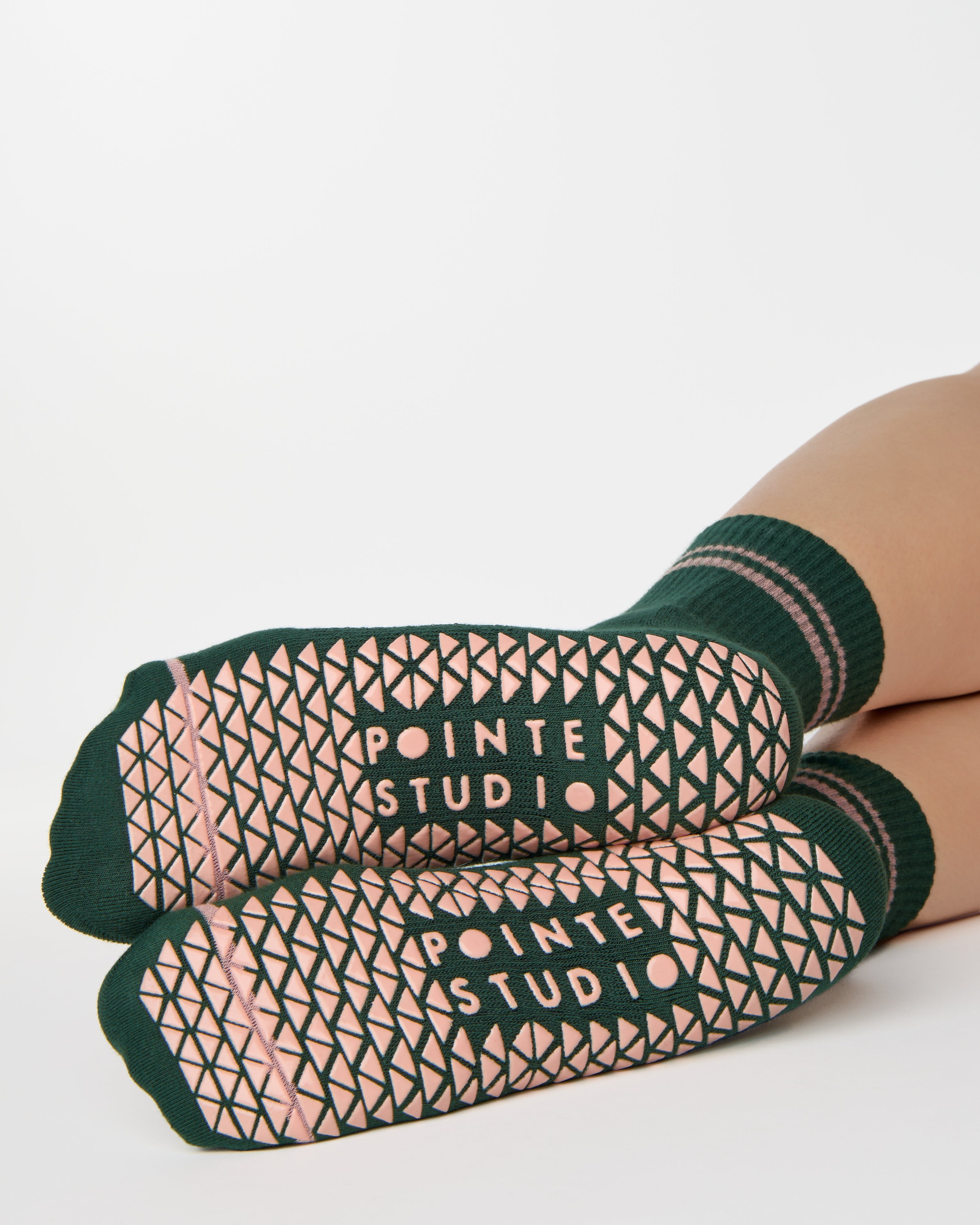 Woman wearing a solid green ankle grip sock with pink stripes on the toes and top ankle cuff made for Pilates, Barre, Yoga, and beyond. 