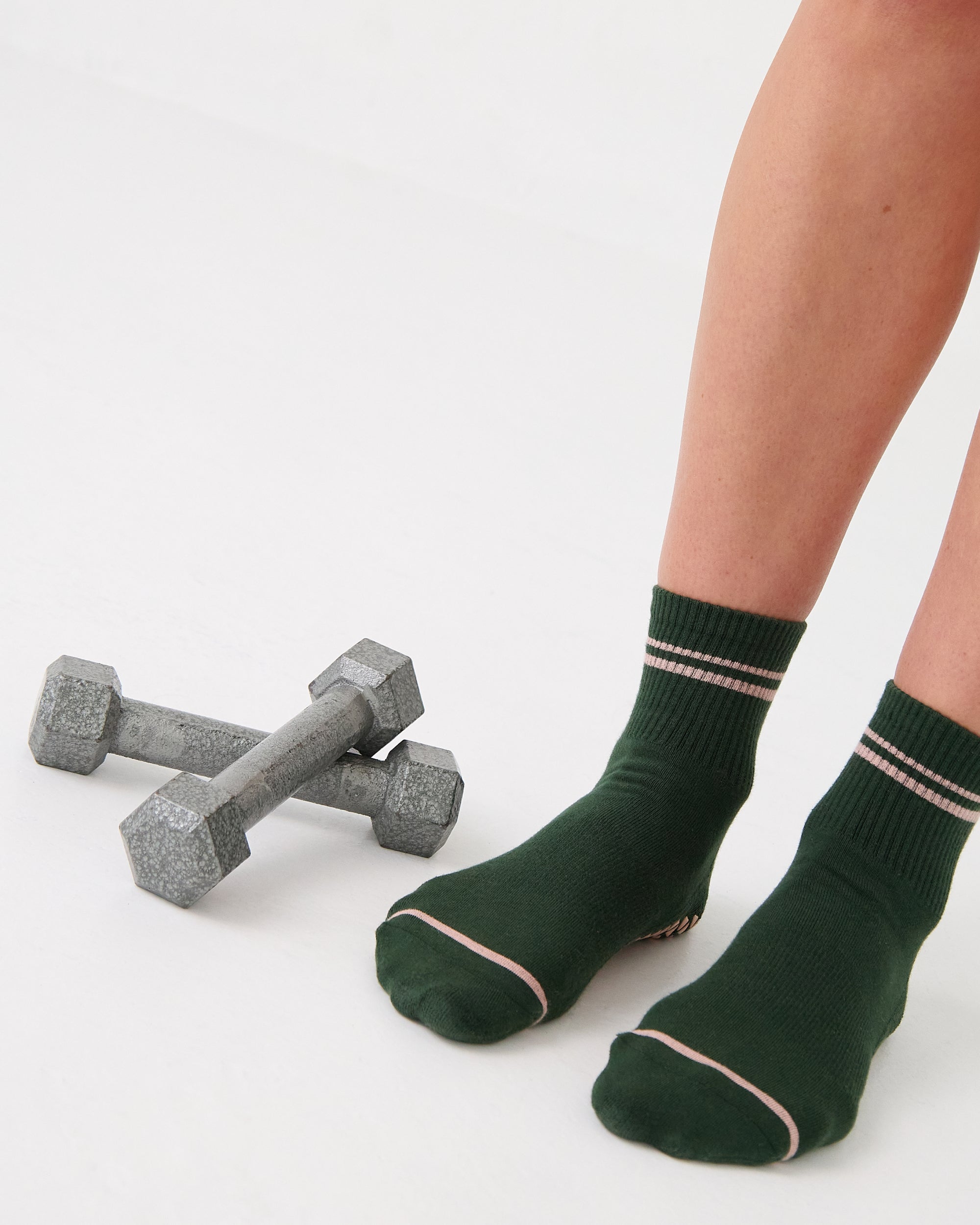 Woman wearing a solid green ankle grip sock with pink stripes on the toes and top ankle cuff made for Pilates, Barre, Yoga, and beyond. 