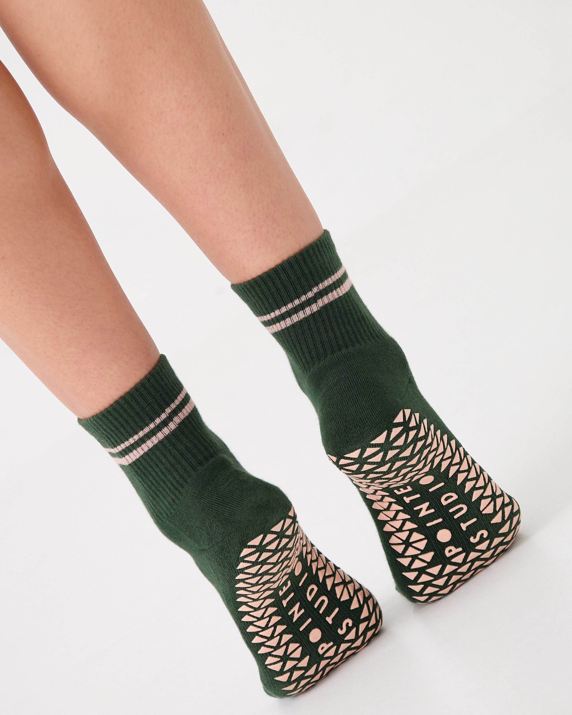 Woman wearing a solid green ankle grip sock with pink stripes on the toes and top ankle cuff made for Pilates, Barre, Yoga, and beyond. 