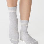 Women wearing a heather grey ankle grip sock with white stripes on the toes and top ankle cuff made for Pilates, Barre, Yoga, and beyond. 
