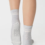 Women wearing a heather grey ankle grip sock with white stripes on the toes and top ankle cuff made for Pilates, Barre, Yoga, and beyond. 