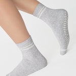 Women wearing a heather grey ankle grip sock with white stripes on the toes and top ankle cuff made for Pilates, Barre, Yoga, and beyond. 