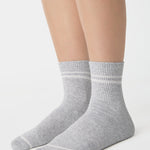 Women wearing a heather grey ankle grip sock with white stripes on the toes and top ankle cuff made for Pilates, Barre, Yoga, and beyond. 