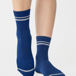 Women wearing a navy blue ankle grip sock with white stripes on the toes and top ankle cuff made for Pilates, Barre, Yoga, and beyond. 