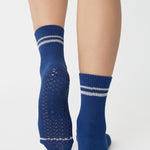 Women wearing a navy blue ankle grip sock with white stripes on the toes and top ankle cuff made for Pilates, Barre, Yoga, and beyond. 