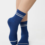 Women wearing a navy blue ankle grip sock with white stripes on the toes and top ankle cuff made for Pilates, Barre, Yoga, and beyond. 